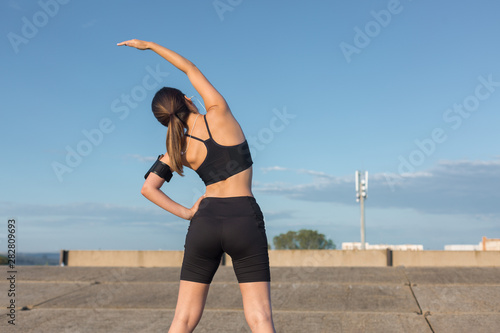 Slim sports girl performs hand pulling exercises on the nature. Enjoys silence and freedom against the blue sky.