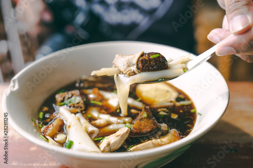 close up Guay jub, gravy noodle soup  thai street food on wooden table with hand and fork photo