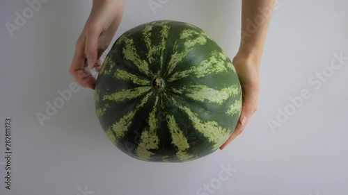 Female hands rotating whole big green striped watermelon on white table. Overhead shot