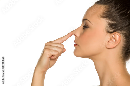 young woman touches her nose with her finger on a white background