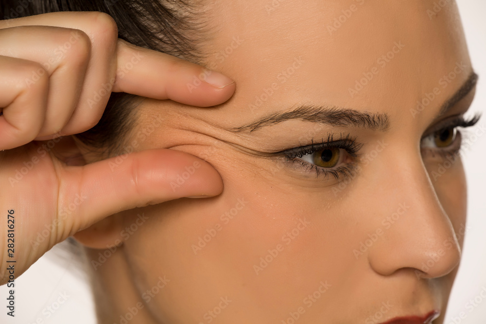 young woman pinching her forehead wrinkles with her fingers on a white background