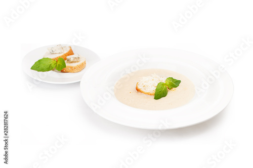 Plate with cream soup with a grenka and pieces of white loaf with cheese and the ground fat on a white saucer. photo