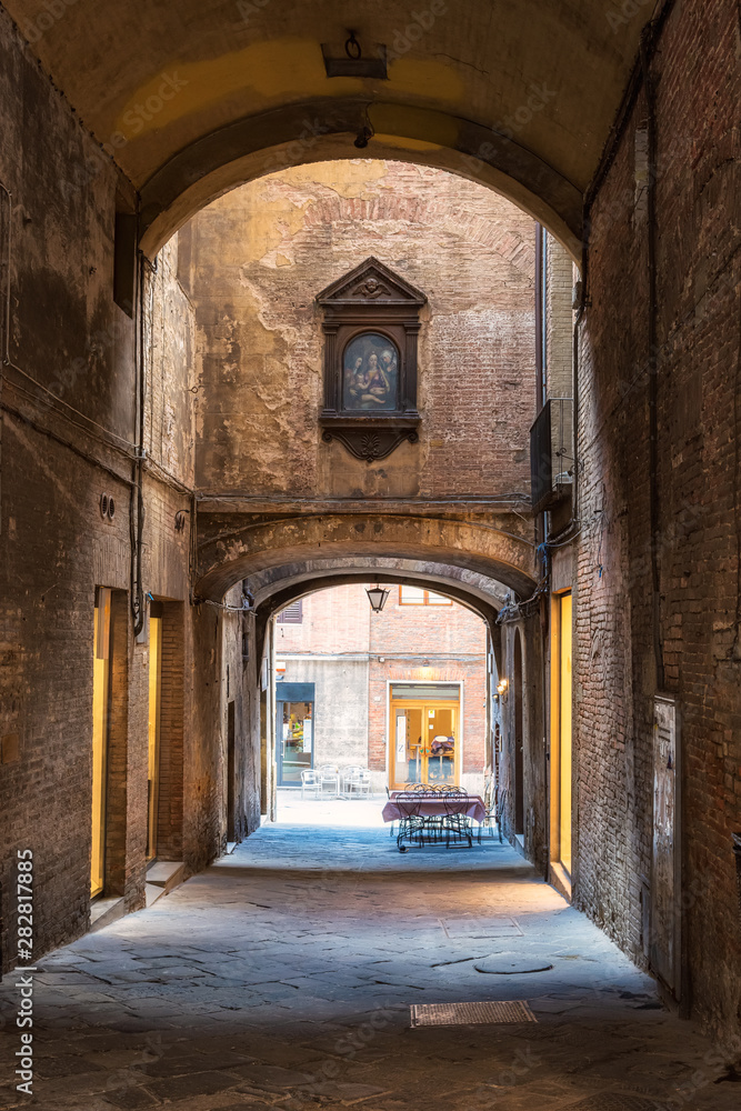 Streets of Siena / Romantic view with Siena medieval narrow streets with high brick walls, arch, iconostasis and an empty restaurant table