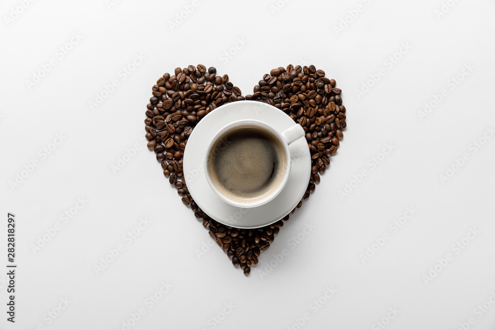 Φωτογραφία top view of tasty coffee in cup on saucer with heart made of coffee grains on wh
