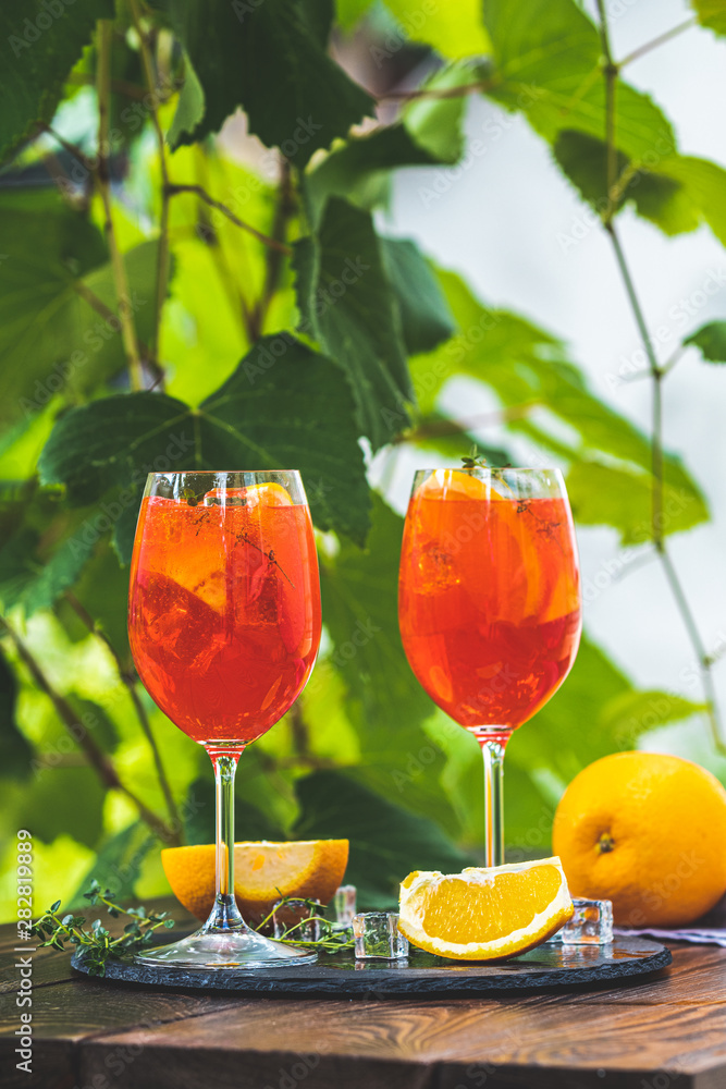 Two Aperol spritz cocktail in big wine glass with oranges, summer Italian  fresh alcohol cold drink. Sunny garden with vineyard background, summer  mood concept, selective focus Stock Photo | Adobe Stock