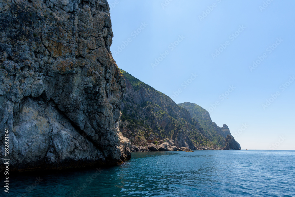 cliff shore from the side of a pleasure boat in the black sea, on a sunny day with clouds in the sky.