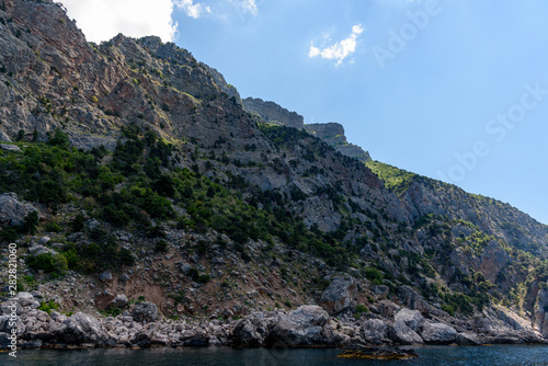 cliff shore from the side of a pleasure boat in the black sea, on a sunny day with clouds in the sky.