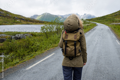 Girl with a backpack walking on an empty road enjoying scenic views. Lake and rocks landscape. Lonely girl. Travel, adventure. Sense of freedom, lifestyle. Explore North Norway. Summer in Scandinavia
