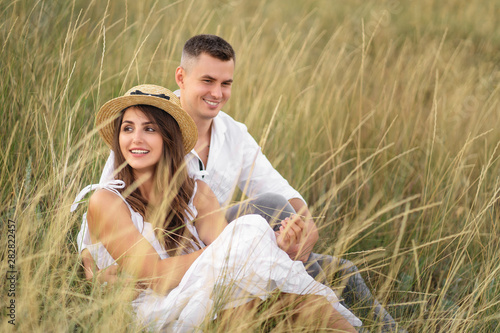 Young couple in love having fun and enjoying the beautiful nature. They sitting at the grass in the meadow