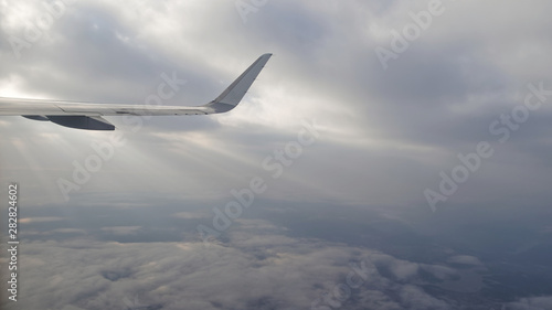 Airplane wing with beautiful white clouds and blue sky background, viewed from the window of an airplane flying above the clouds during sunset.