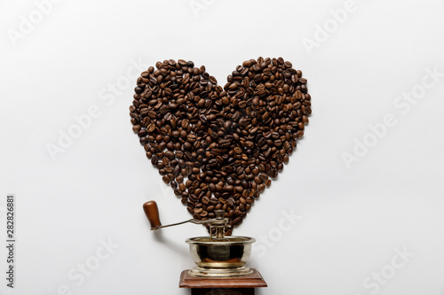 top view of heart made of coffee grains near vintage coffee grinder on white background