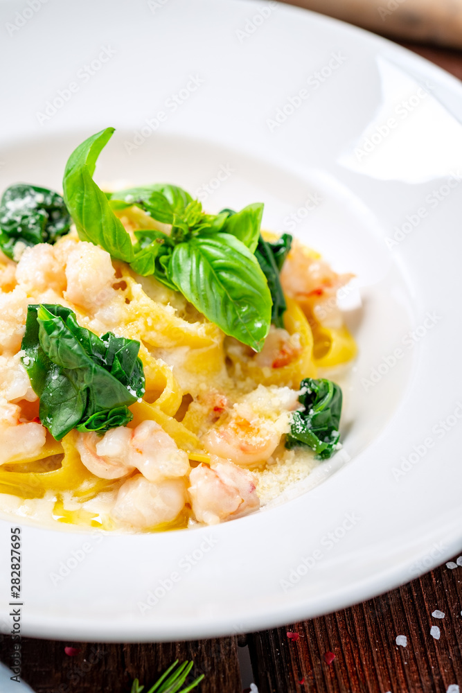 Tagliatelle with seafood. Traditional Italian pasta with shrimp, Basil in cream sauce on a white plate. Macro