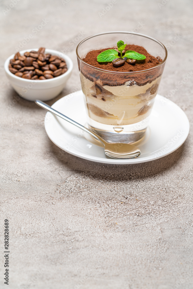 Classic tiramisu dessert in a glass cup on plate and coffee beans on concrete background Classic tiramisu dessert in a glass cup on plate and coffee beans on concrete background