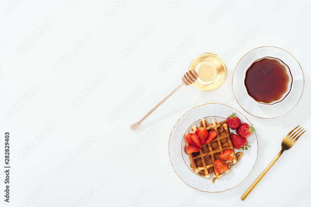 Fototapeta premium top view of delicious breakfast with waffle, strawberries and tea on white