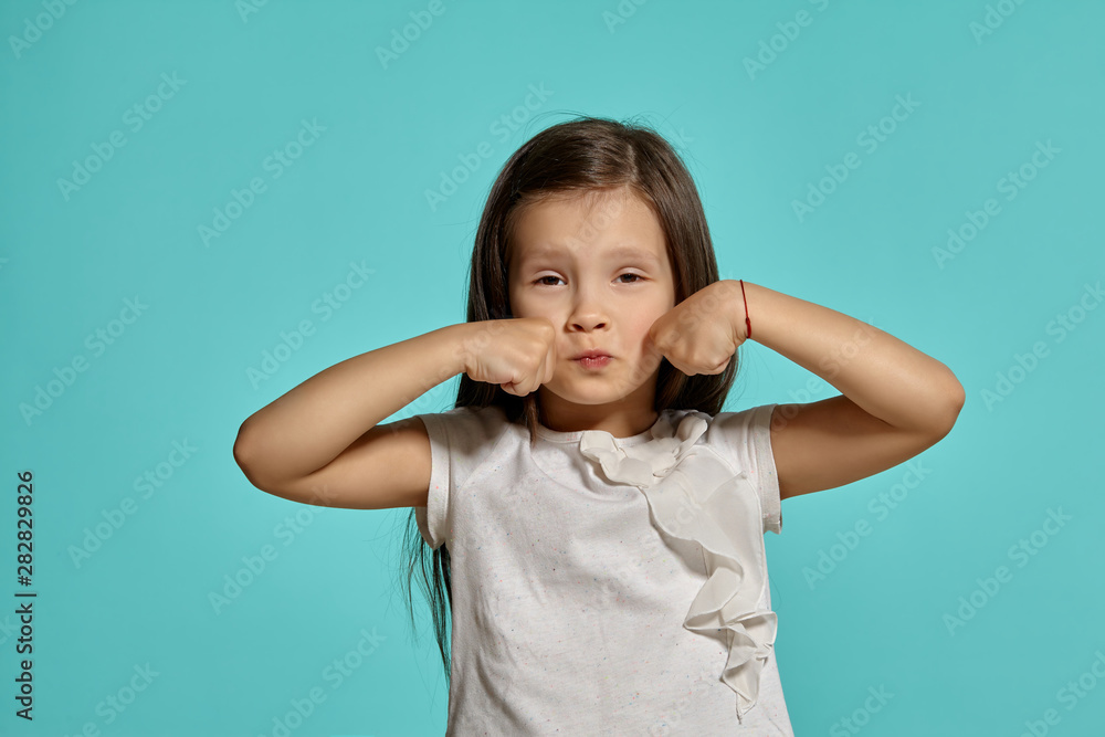 Close-up studio shot of beautiful brunette little girl posing against a blue background. Close-up studio shot of beautiful brunette little girl posing against a blue background.