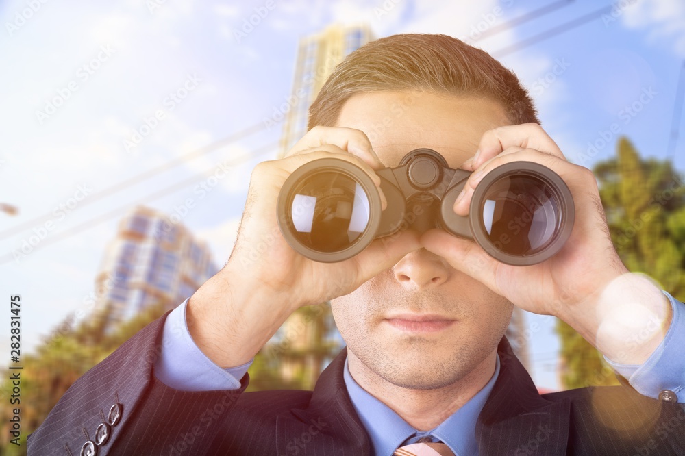 Businessman looking through binoculars against the blurred city