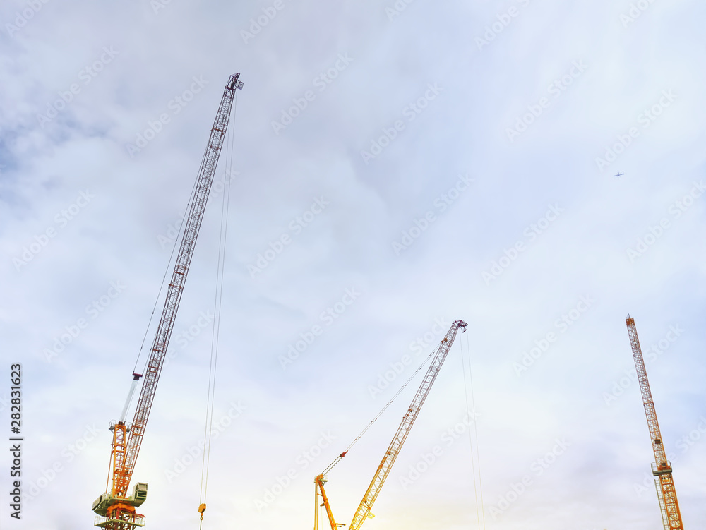 Group of Construction Cranes with Boom Structure Pointing Up Against Cloudy Sky Group of Construction Cranes with Boom Structure Pointing Up Against Cloudy Sky