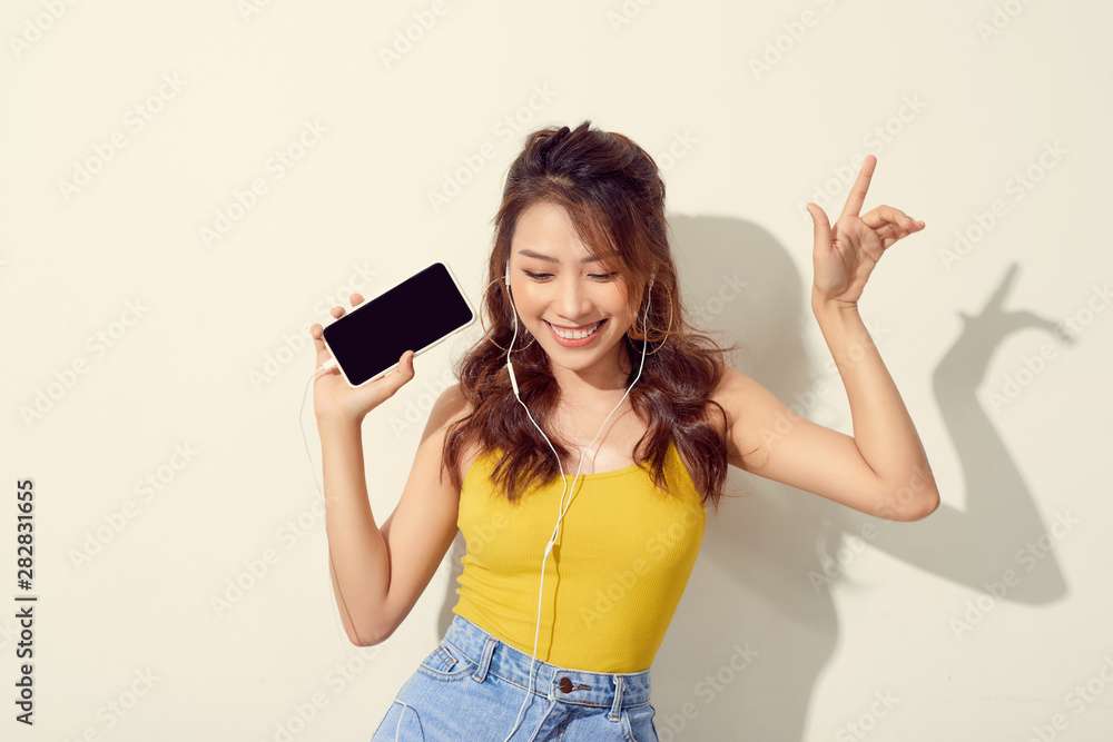 Portrait of a cheerful beautiful girl showing or presenting mobile phone application and pointing finger to sky