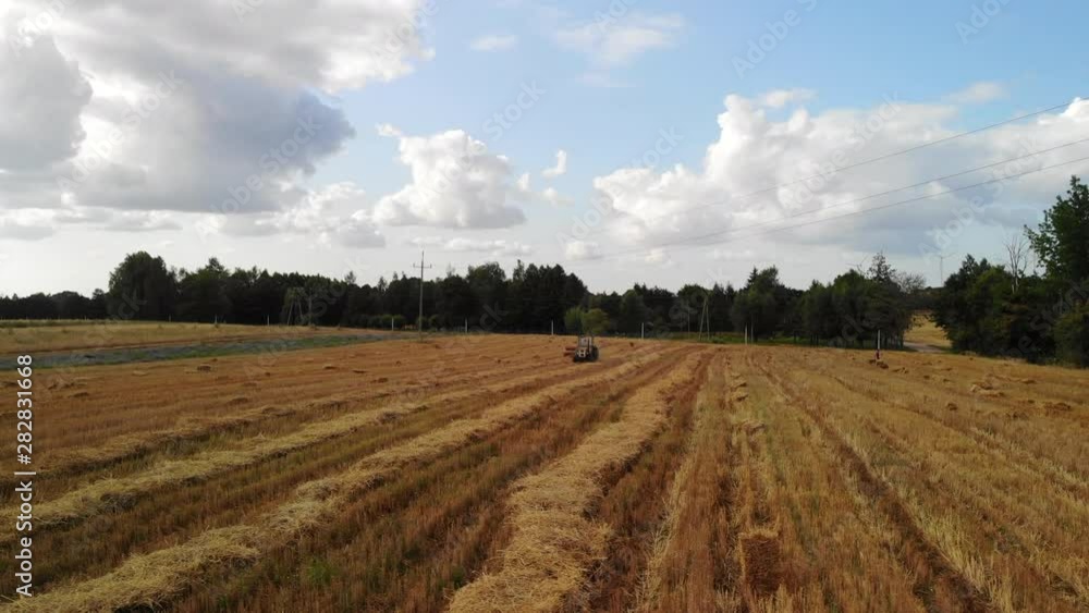 Hay stack cubes in wheat field. Aerial flight view of a cube baler tractor discharges a fresh wheat bale during harvesting. Hay stack cubes in wheat field. Aerial flight view of a cube baler tractor discharges a fresh wheat bale during harvesting.