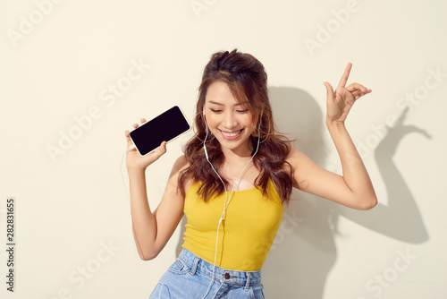 Portrait of a cheerful beautiful girl showing or presenting mobile phone application and pointing finger to sky