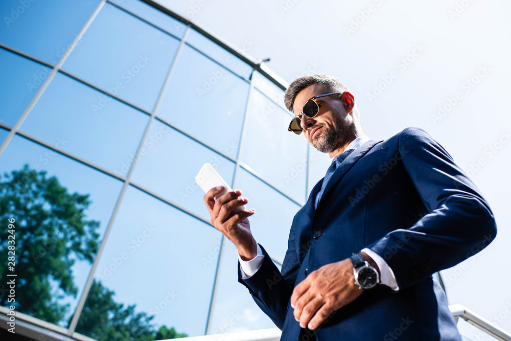 low angle view of handsome man in suit and glasses using smartphone low angle view of handsome man in suit and glasses using smartphone