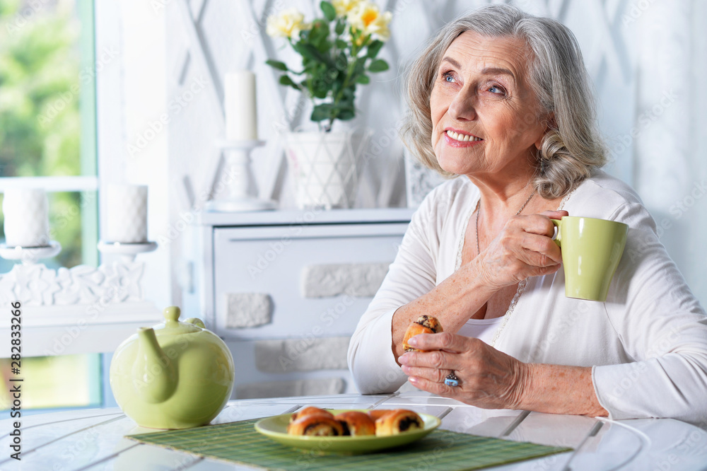 Portrait of beautiful smiling senior woman drinking tea while sitting at kitchen table Portrait of beautiful smiling senior woman drinking tea while sitting at kitchen table