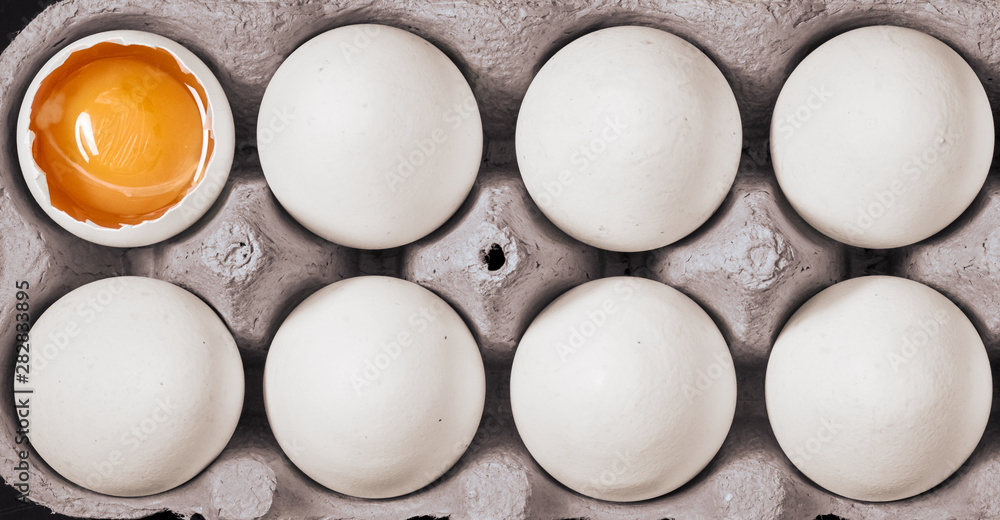 Top view of white eggs and one cracked egg in box Top view of white eggs and one cracked egg in box