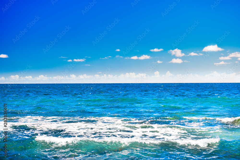 Seascape with blue water surface, calm waves, bright sky and white clouds