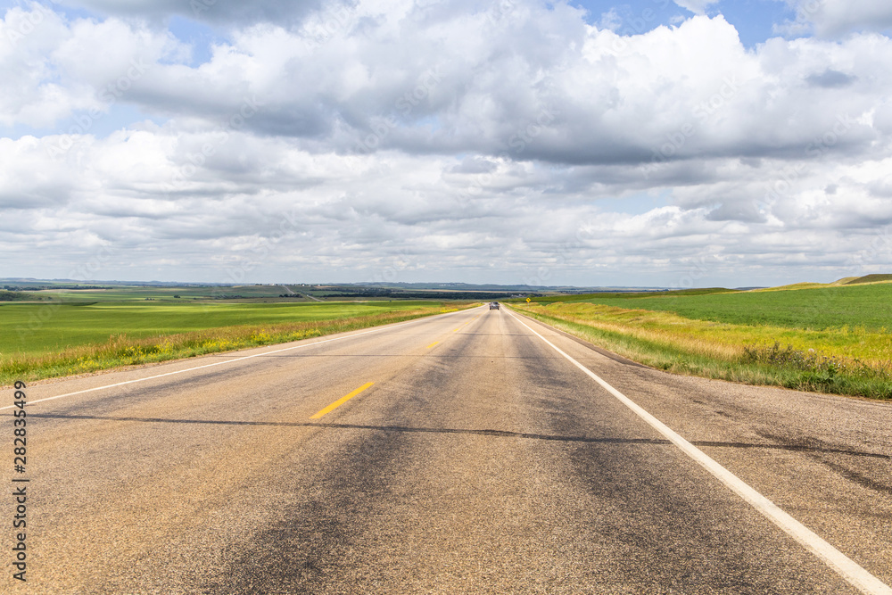 a long dirt road in rural North Dakota with a bright blue sky with clouds in the horizon