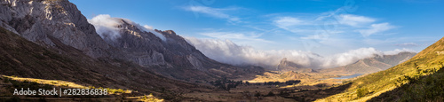 Panoramic photo in the valley of Arbas in Leon, Spain, with clouds passing over the peaks towards the valley photo