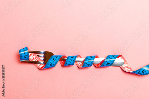 Top view of obesity concept with fork wrapped in measuring tape on blue background