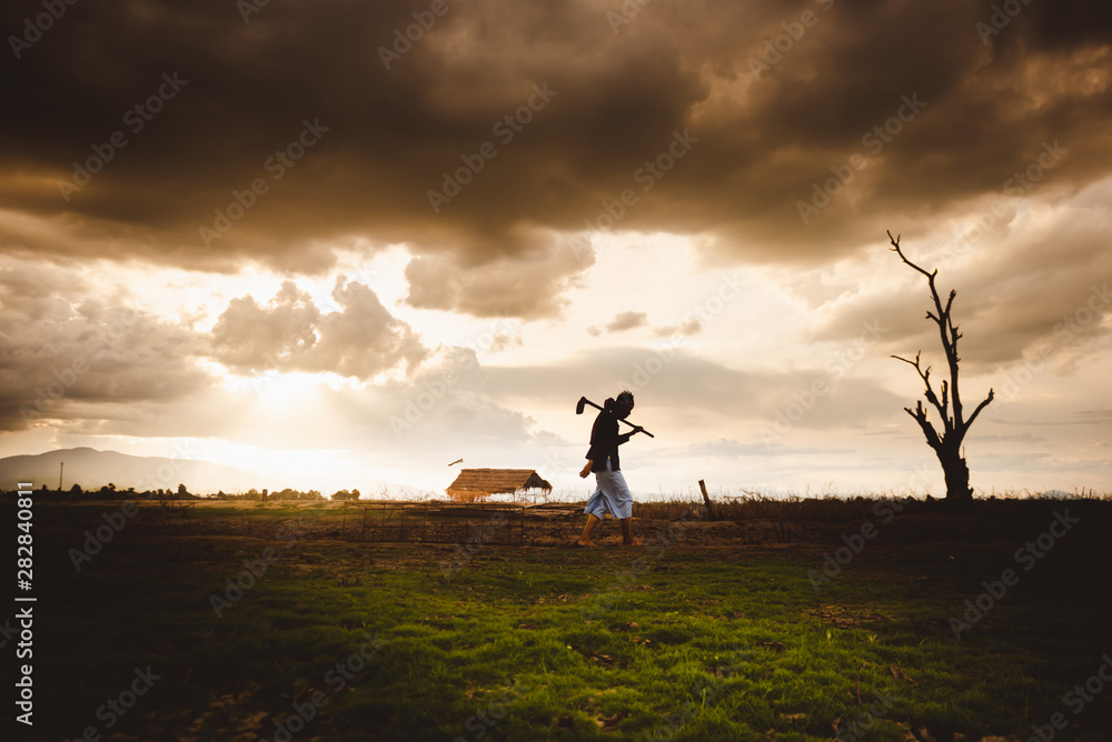 Hopeless and lonely Farmer carrying hoe and walking through his dry field at sunset. Global warming crisis,  Economic crisis concept.