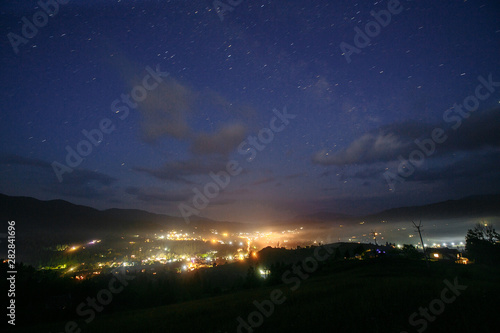 starry sky over a mountain town with night lights