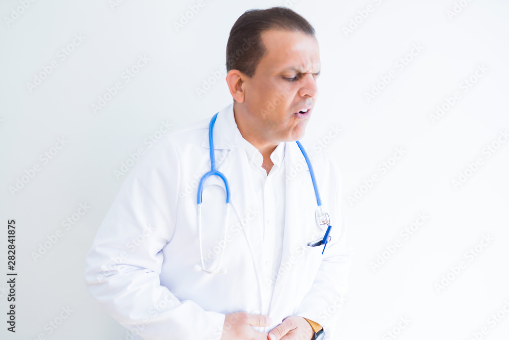 Middle age doctor man wearing stethoscope and medical coat over white background with hand on stomach because nausea, painful disease feeling unwell. Ache concept. Middle age doctor man wearing stethoscope and medical coat over white background with hand on stomach because nausea, painful disease feeling unwell. Ache concept.