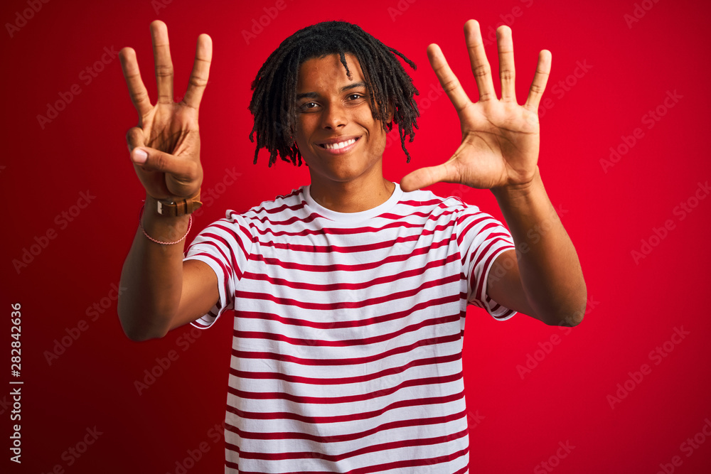 Young afro man with dreadlocks wearing striped t-shirt standing over isolated red background showing and pointing up with fingers number eight while smiling confident and happy. Young afro man with dreadlocks wearing striped t-shirt standing over isolated red background showing and pointing up with fingers number eight while smiling confident and happy.
