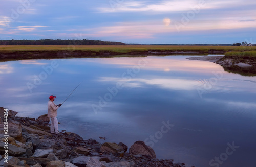 Fisherman catches fish at dusk on a break of river in forest. Dark gloomy photo. USA. Maine. fishing in the USA.
