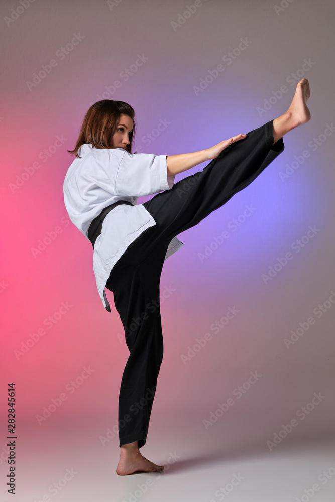 Obraz premium Athletic woman in traditional kimono is practicing karate in studio.