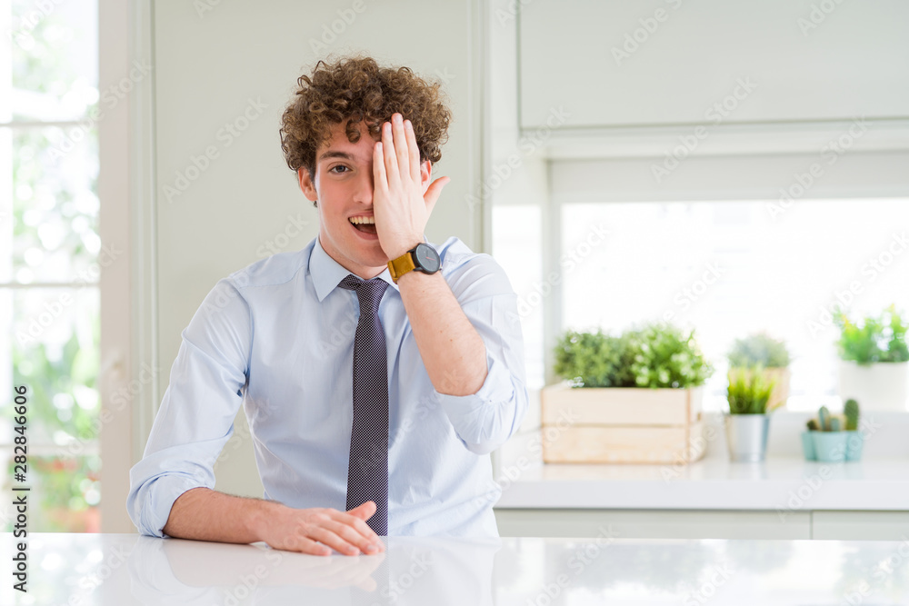 Young business man wearing a tie covering one eye with hand with confident smile on face and surprise emotion.