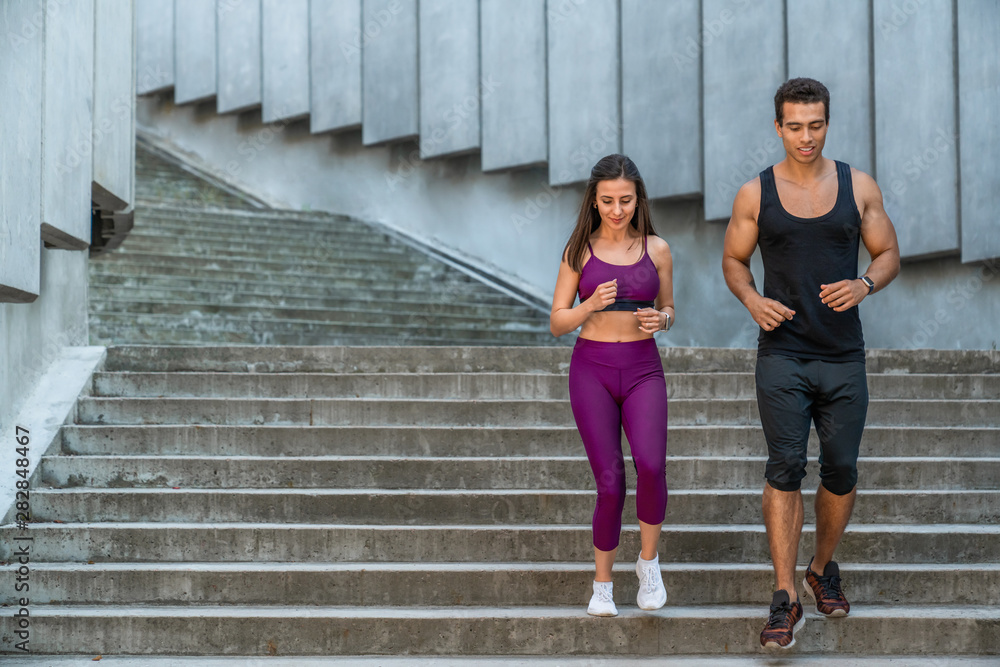 Young sports couple jogging down the stairs in the urban environment at morning