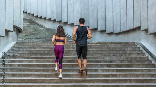 Rear view of fit woman and man running up the stairs in the city