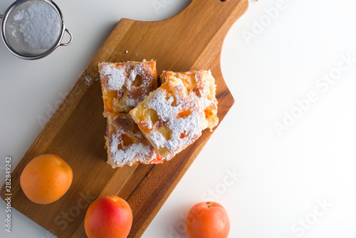 Top view of homemade apricot cake dicey slices with sugar powder on it, on the wooden board and sieve photo