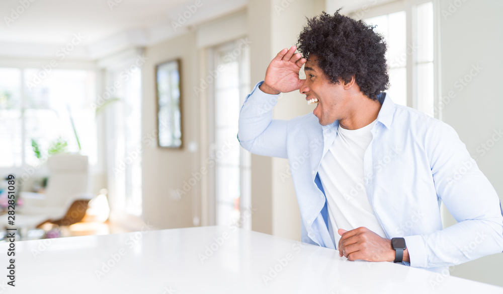 African American man at home very happy and smiling looking far away with hand over head. Searching concept.