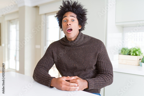 African American man wearing winter sweater afraid and shocked with surprise expression, fear and excited face. © Krakenimages.com