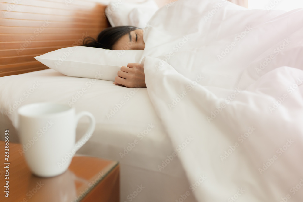 Woman stretching in bed after waking up, back view. Woman sitting near the big white window while stretching on bed after waking up with sunrise at morning, back view.