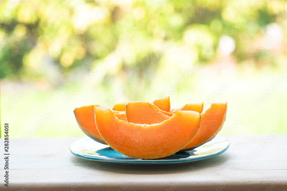 Pieces of juicy fresh cantaloupe melon on a wooden table against the background of the garden. Selective focus, bokeh, copy space. Bright summer sunny background with food. Pieces of juicy fresh cantaloupe melon on a wooden table against the background of the garden. Selective focus, bokeh, copy space. Bright summer sunny background with food.