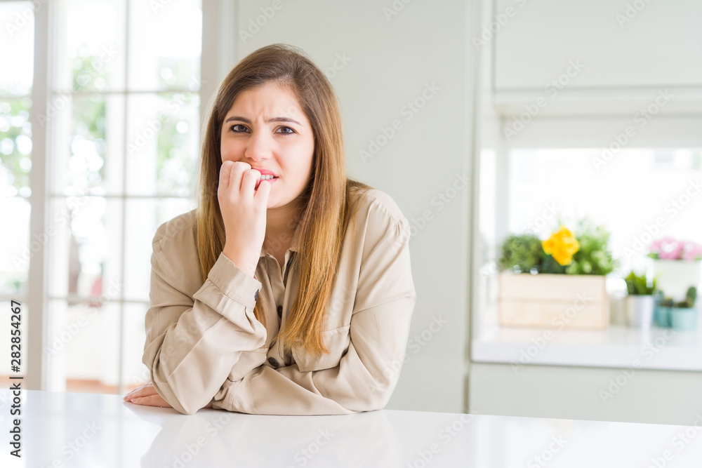Beautiful young woman at home looking stressed and nervous with hands on mouth biting nails. Anxiety problem. Beautiful young woman at home looking stressed and nervous with hands on mouth biting nails. Anxiety problem.