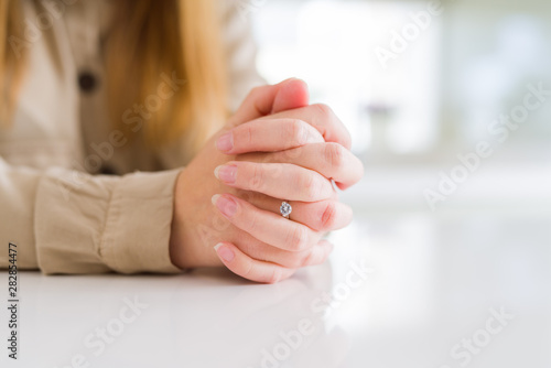 Close up of woman finger showing engagement ring with crossed hands over white table