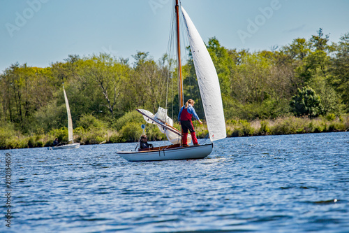 Sail boat racing gala on Wroxham Broad, Norfolk. A female sailor walks along the deck to adjust the foresail whilst her male partner steers the boat during a frantic race on Wroxham Broad, Norfolk. photo