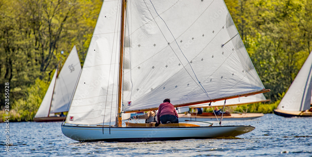 Sail boat racing gala on Wroxham Broad, Norfolk. A male sailor moving around his brown boat during a frantic race on the Norfolk Broads proving that sailing is physical and not a sedate activity. Sail boat racing gala on Wroxham Broad, Norfolk. A male sailor moving around his brown boat during a frantic race on the Norfolk Broads proving that sailing is physical and not a sedate activity.