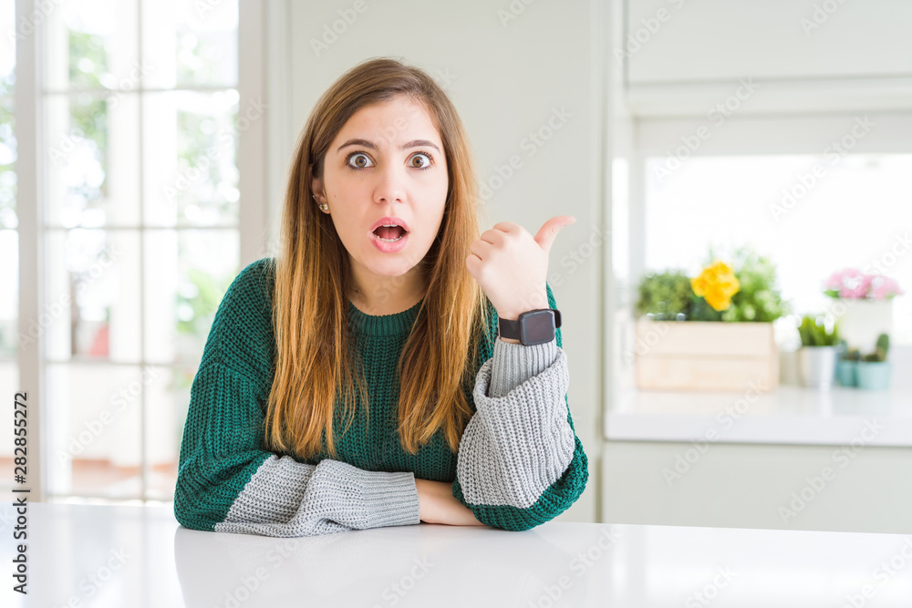 Young beautiful plus size woman wearing casual striped sweater Surprised pointing with hand finger to the side, open mouth amazed expression.